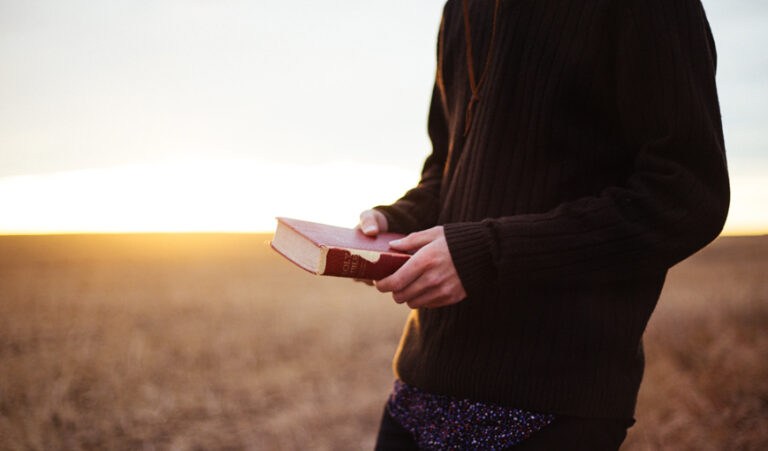 Man holding bible in a sunny field.